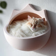 3D printed crown-shaped wall mounted cat bed in matte blush PLA with a fluffy cream cat sleeping inside.