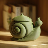 3D printed snail-shaped memorial urn with removable lid in matte PLA displayed on a wooden shelf in a cozy modern interior.