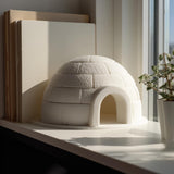 3D printed white igloo shelf decor with textured brick pattern displayed on a modern desk beside books and indoor plants.