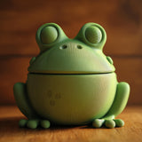 3D printed frog memorial urn with large eyes and removable lid displayed on a wooden tabletop in warm natural lighting.