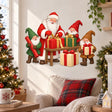 Santa and three smiling gnomes holding and wrapping red, green and gold Christmas gifts around a small wooden table.