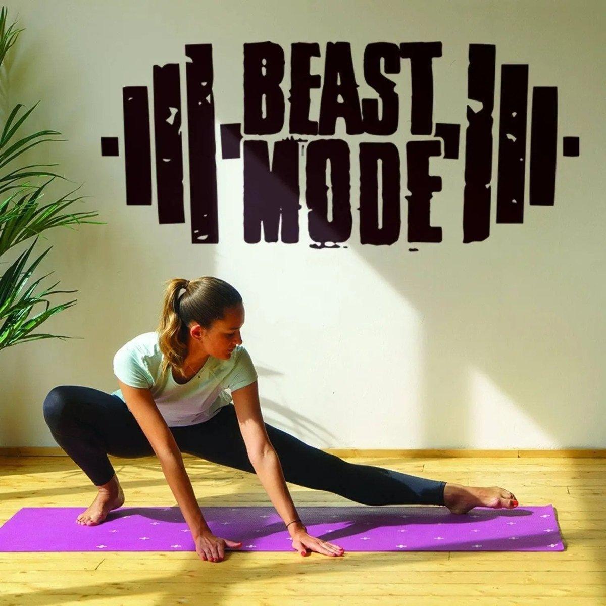 Женщина на коврике рядом с настенной фразой Beast Mode