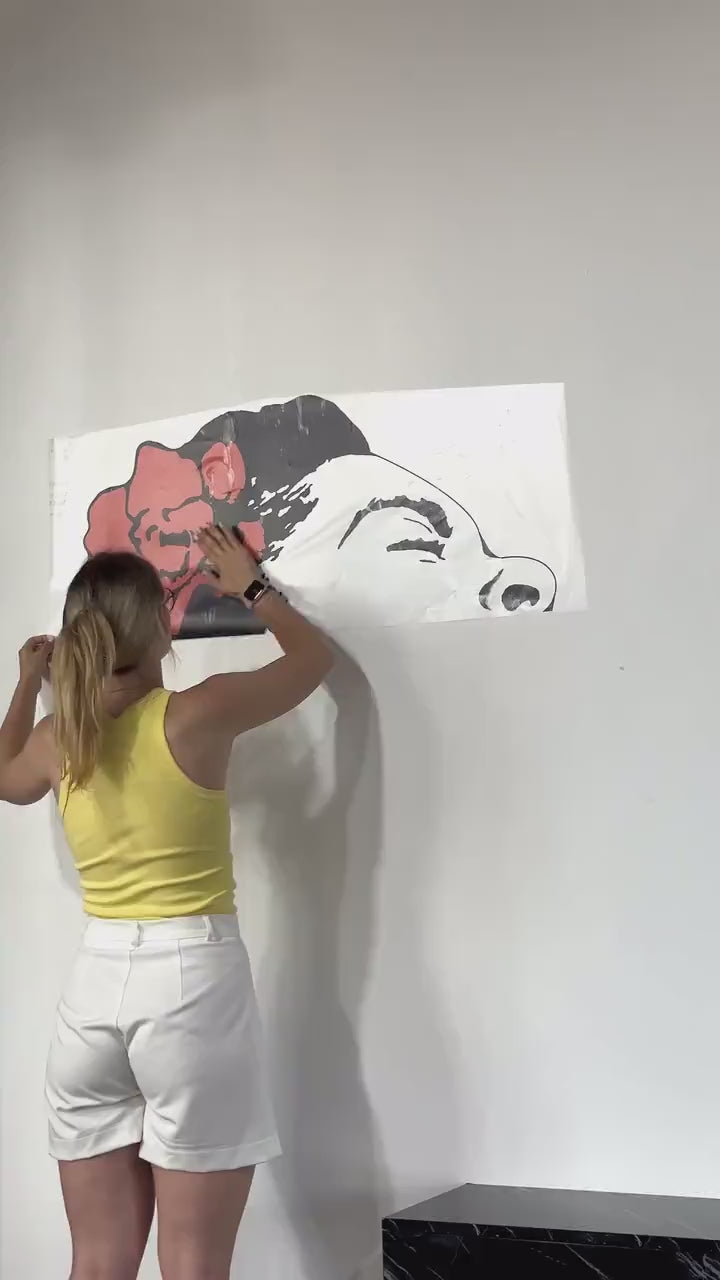Woman applying a singing woman street-art wall decal with a flower design.