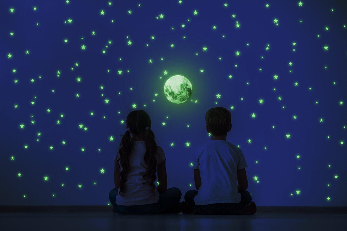 Children admiring glowing star stickers and a moon decal on a dark wall, creating a magical night sky.