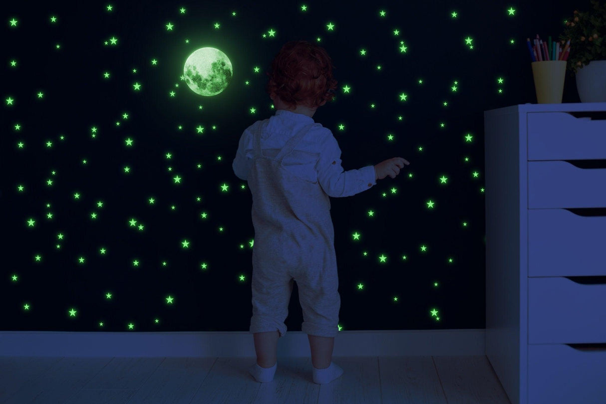 Child admiring glowing star stickers and moon wall decals in a darkened room, creating a magical night sky.