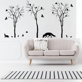 Botanical wildlife vinyl decal set featuring tree silhouettes, birds, and animals above a modern sofa in stylish interior.