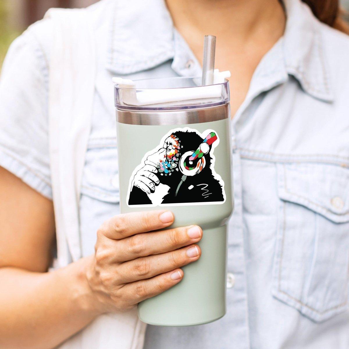 Person holding a tumbler with a colorful monkey design sticker.