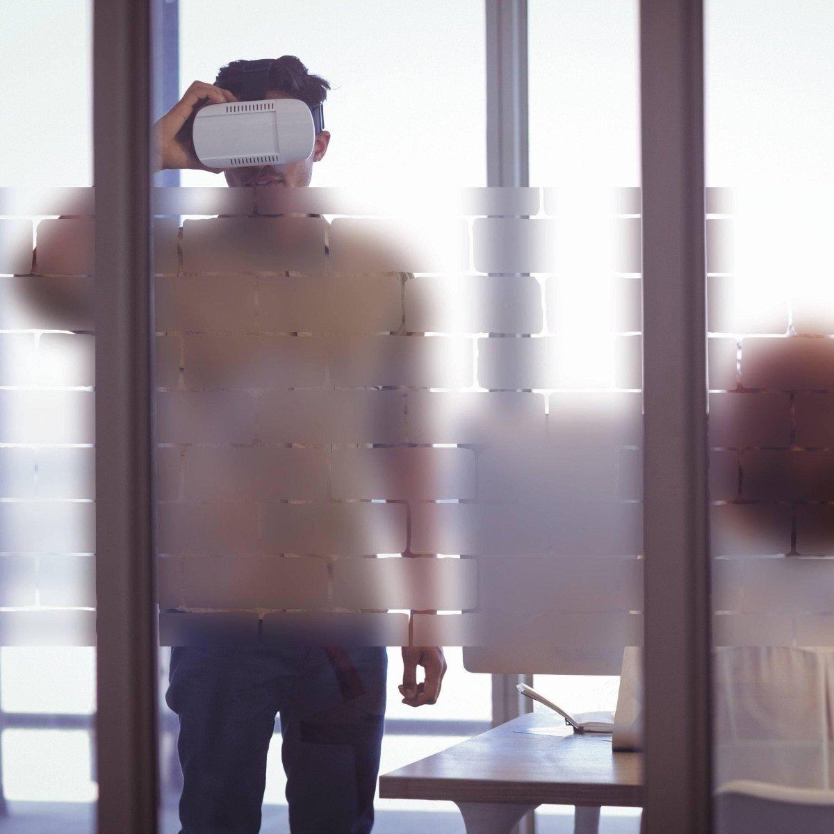 Man in an office wearing VR headset behind frosted window film for privacy and natural light.