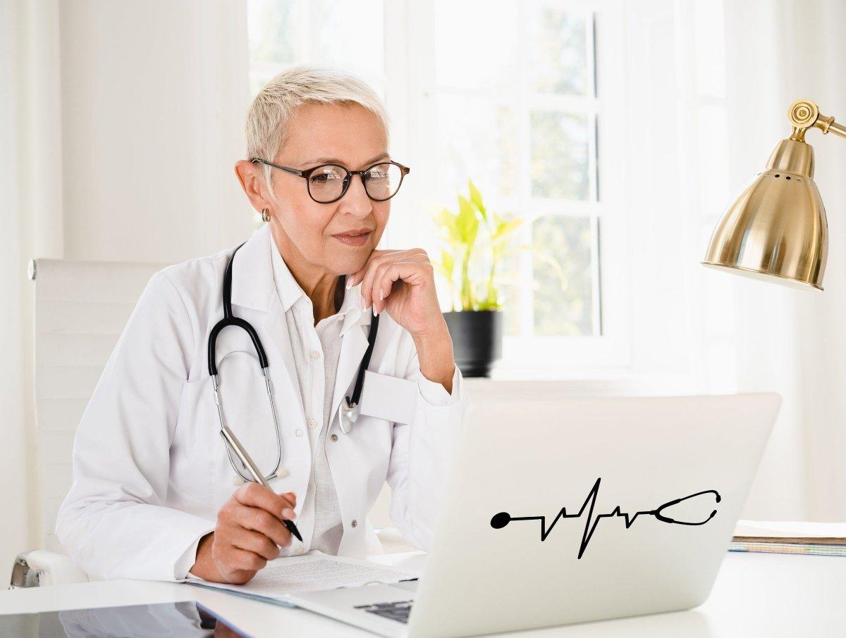 Experienced doctor with stethoscope working on laptop, showcasing a heartbeat sticker.