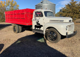 Vintage farm truck with red bed and farm animal silhouette decal on a rural landscape.
