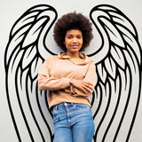 Young woman posing with angel wings wall decor in a stylish bohemian setting, showcasing artistic wall art.