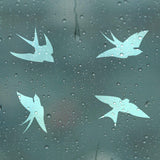 Four blue bird decals on a rain-soaked window, promoting bird safety and collision awareness.