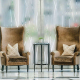 Elegant living room scene with two plush armchairs and a glass side table, featuring frosted glass window decor.