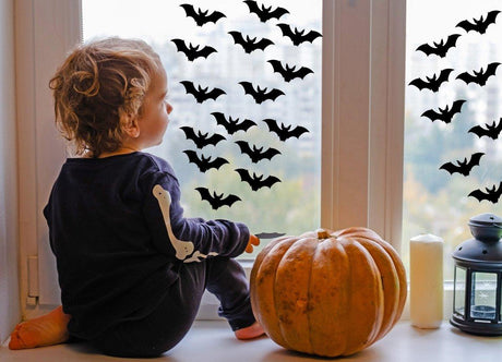 Child sitting by window with Halloween bat decals and a pumpkin, creating a spooky atmosphere.