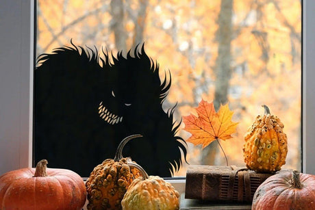 Spooky monster silhouette vinyl decal on window with pumpkins and autumn leaves.