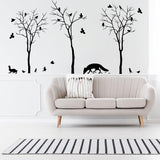 Elegant wall decals of trees and animals in a cozy living room with a modern sofa and striped rug.
