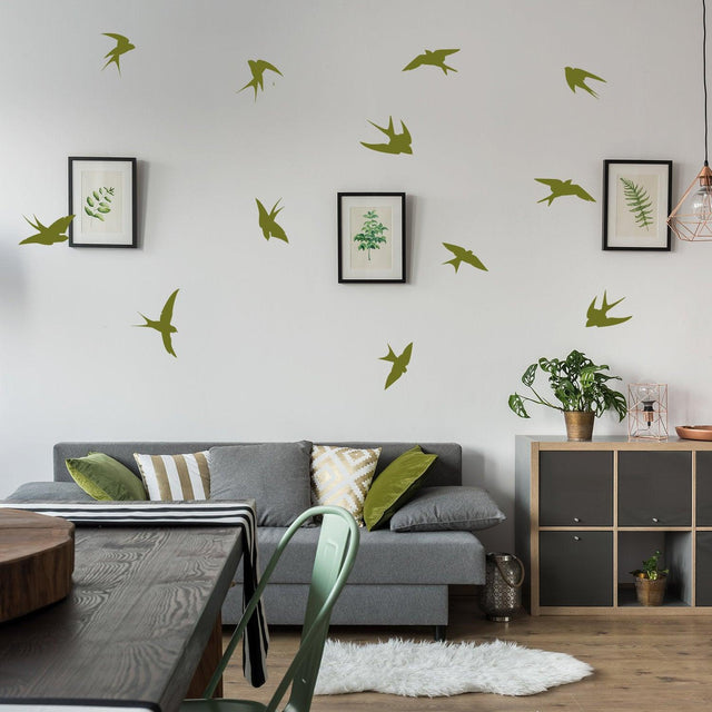 12 flock of birds wall stickers in green vinyl above a living room couch with plants and artwork.
