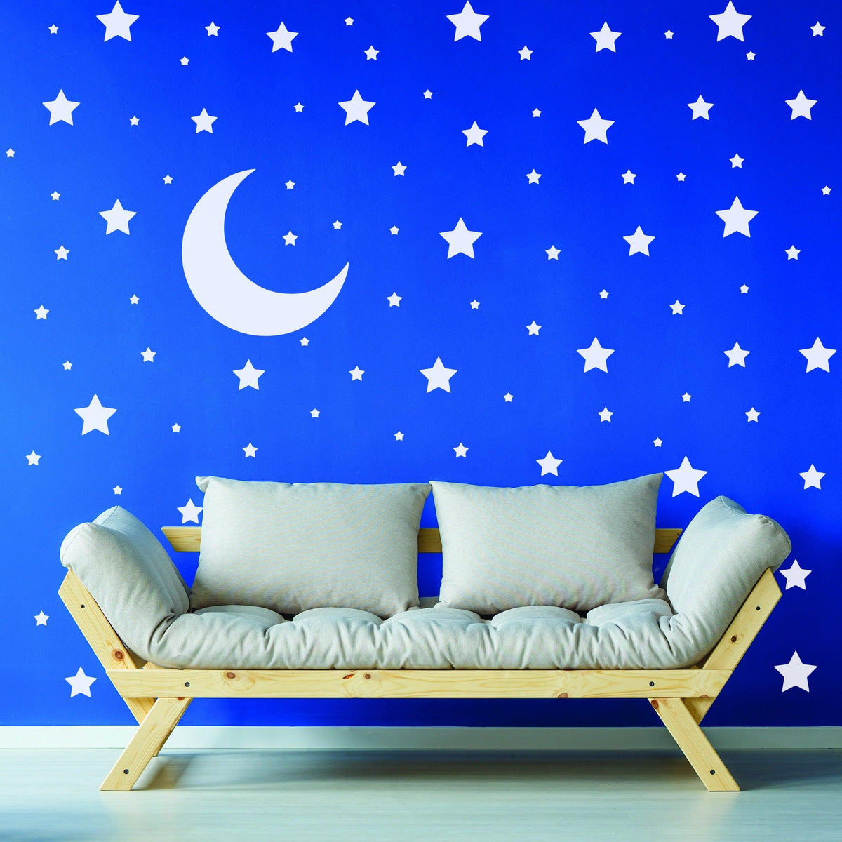 Blue nursery wall with white star and moon stickers above a wooden sofa.