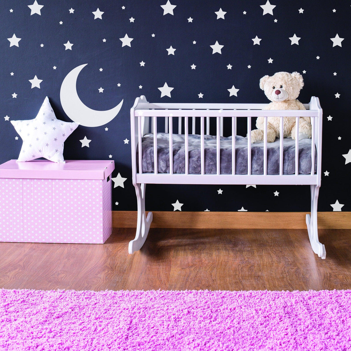 Baby nursery with white stars wall stickers, a moon design, and a crib with a teddy bear.