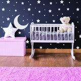 Baby nursery with white stars wall stickers, a moon design, and a crib with a teddy bear.