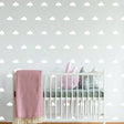 Nursery with white cloud wall decals above a crib featuring pink and gray plush toys and a cozy blanket.