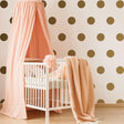 Stylish nursery featuring 40 gold circle wall decals, a white crib, and soft pink textiles for a cozy decor.