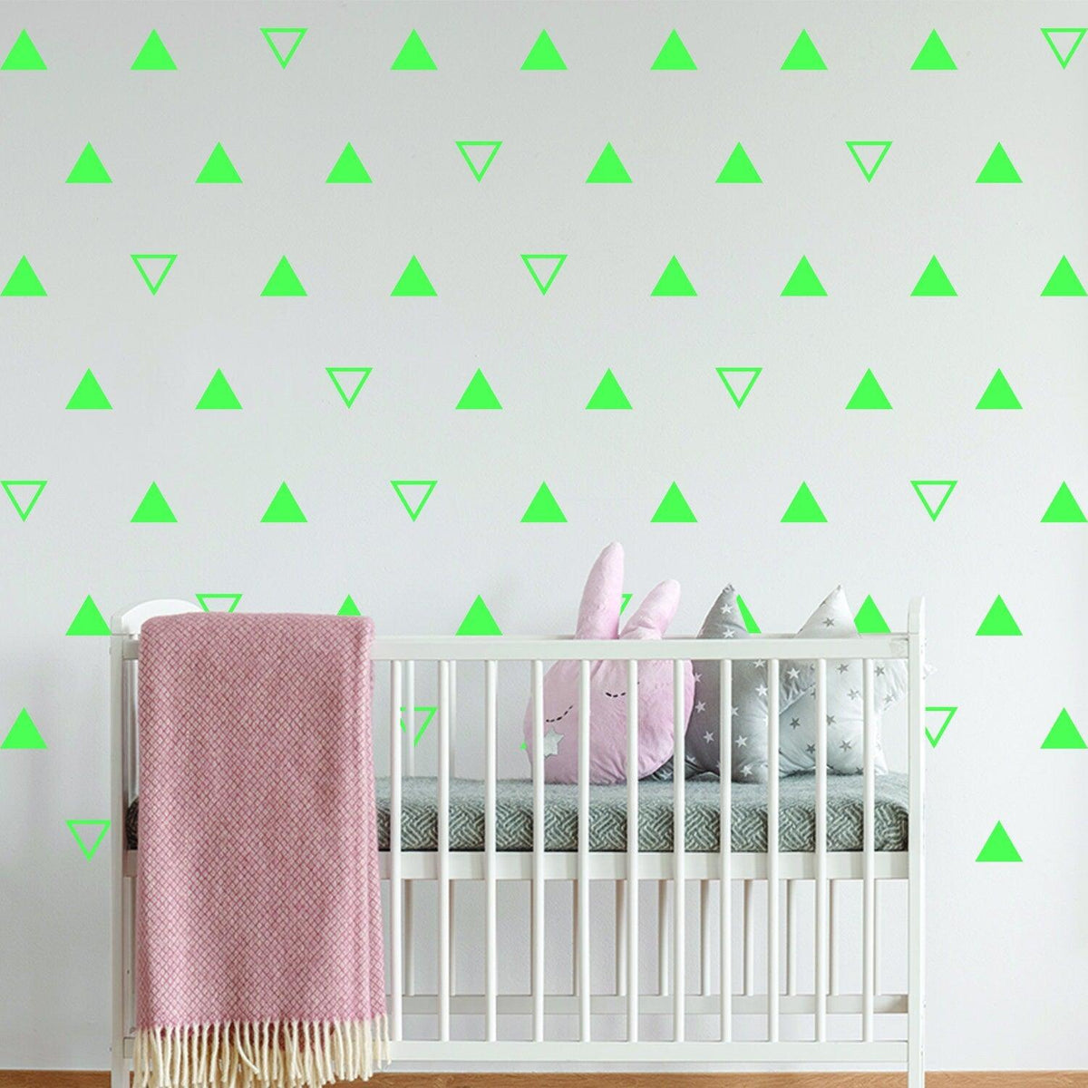 Nursery wall decor with green triangle vinyl decals and a crib featuring soft toys and a pink blanket.