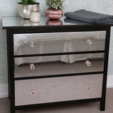 Modern black dresser with mirrored drawers, decorative plant, and cozy gray throw, enhancing contemporary interior design.