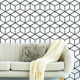 Geometric black and white hexagon honeycomb wall mural in modern living room with cozy sofa and decorative throw.