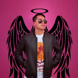 Person wearing sunglasses in front of pink angel wings mural with halo, styled against a vibrant background.