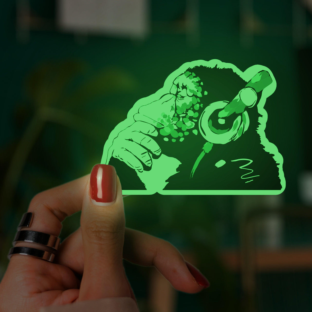Glow in the dark monkey vinyl sticker held in hand, featuring headphones and musical themes, vibrant green design.