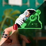 Glow in the dark monkey vinyl sticker held in hand, featuring playful design with headphones and vibrant colors.