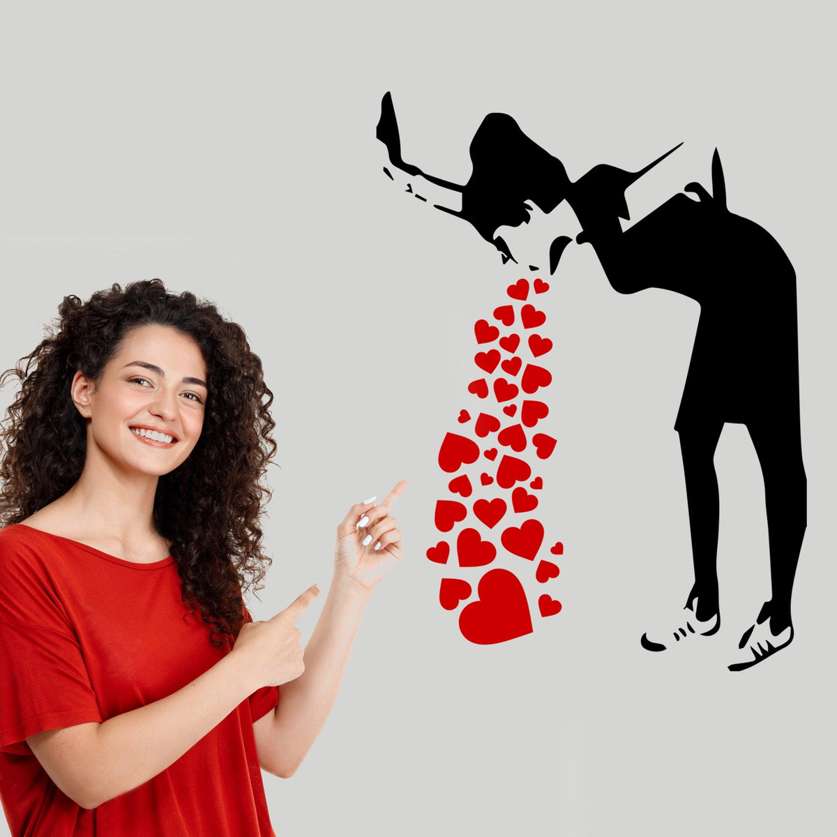 Woman pointing at a street-art Love Sick Girl wall decal with red hearts.
