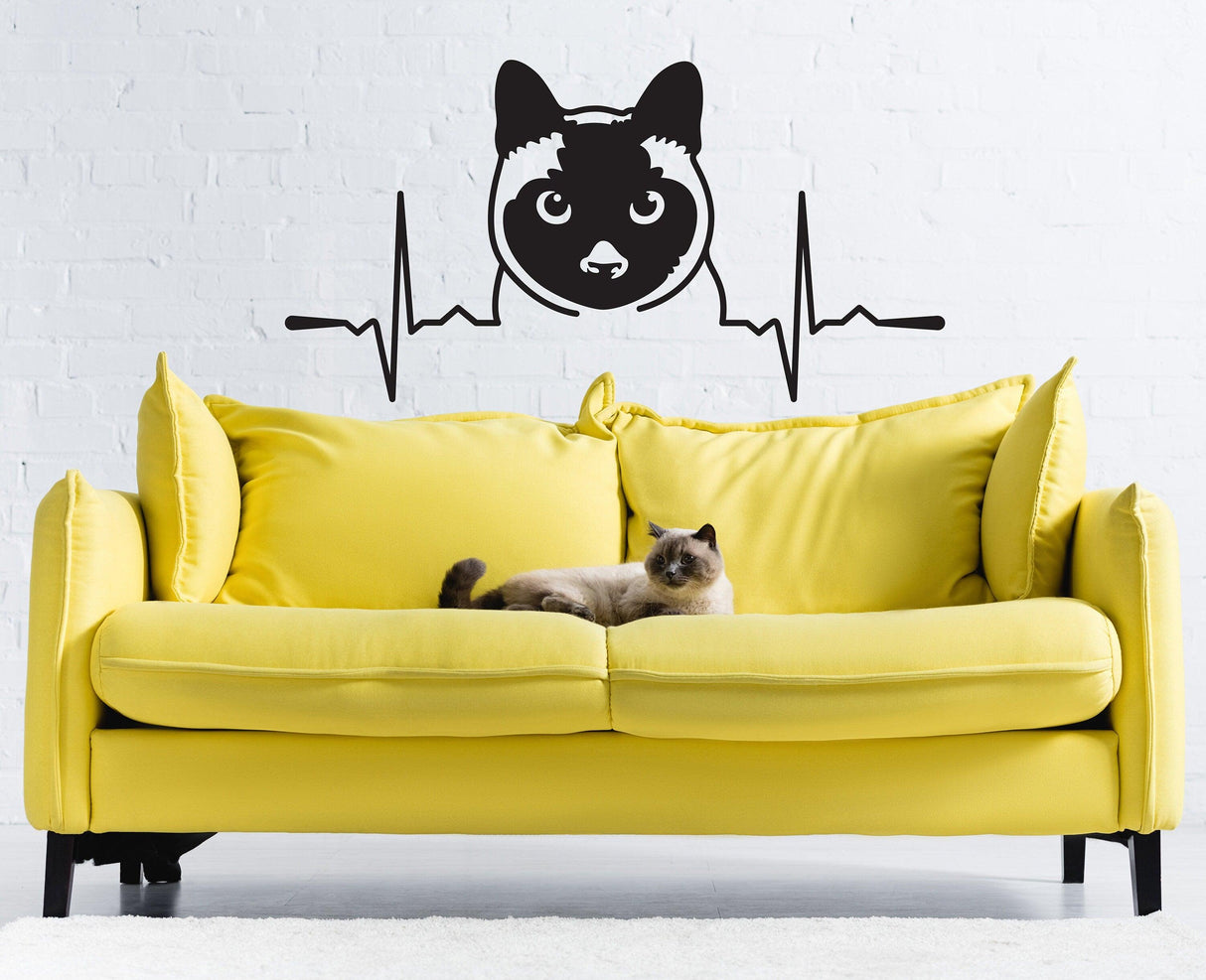Siamese cat wall sticker design above a yellow couch with a real cat resting on it.