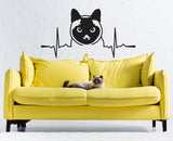 Siamese cat wall sticker design above a yellow couch with a real cat resting on it.