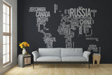 Custom wall art featuring a world map design made of country names on a dark wall above a cozy gray sofa.