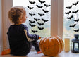 Child looking out the window decorated with Halloween bats decals and a pumpkin beside them.