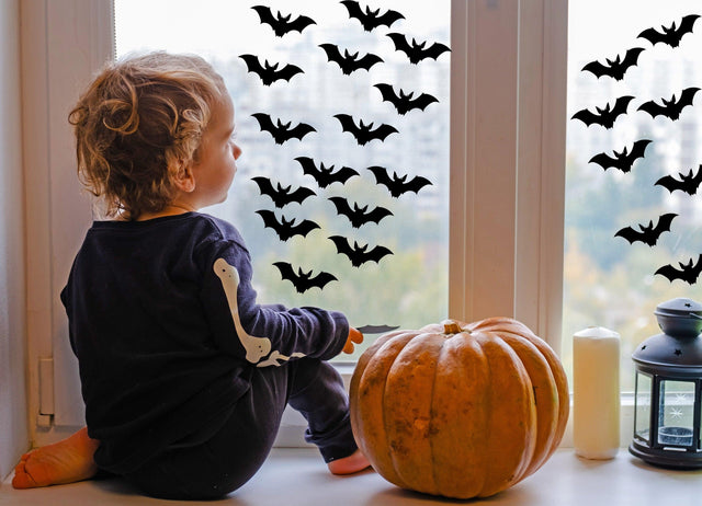 Child looking out the window decorated with Halloween bats decals and a pumpkin beside them.