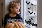 Child looking out window decorated with Halloween bats and pumpkins decals, celebrating the spooky season.