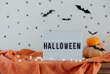 Halloween decor with spider wall decals, lightbox sign, pumpkin, and bat accents for festive atmosphere.