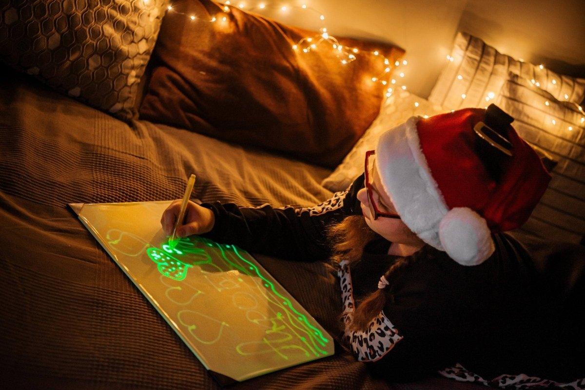 Ребёнок в новогодней шапке рисует светящиеся изображения.